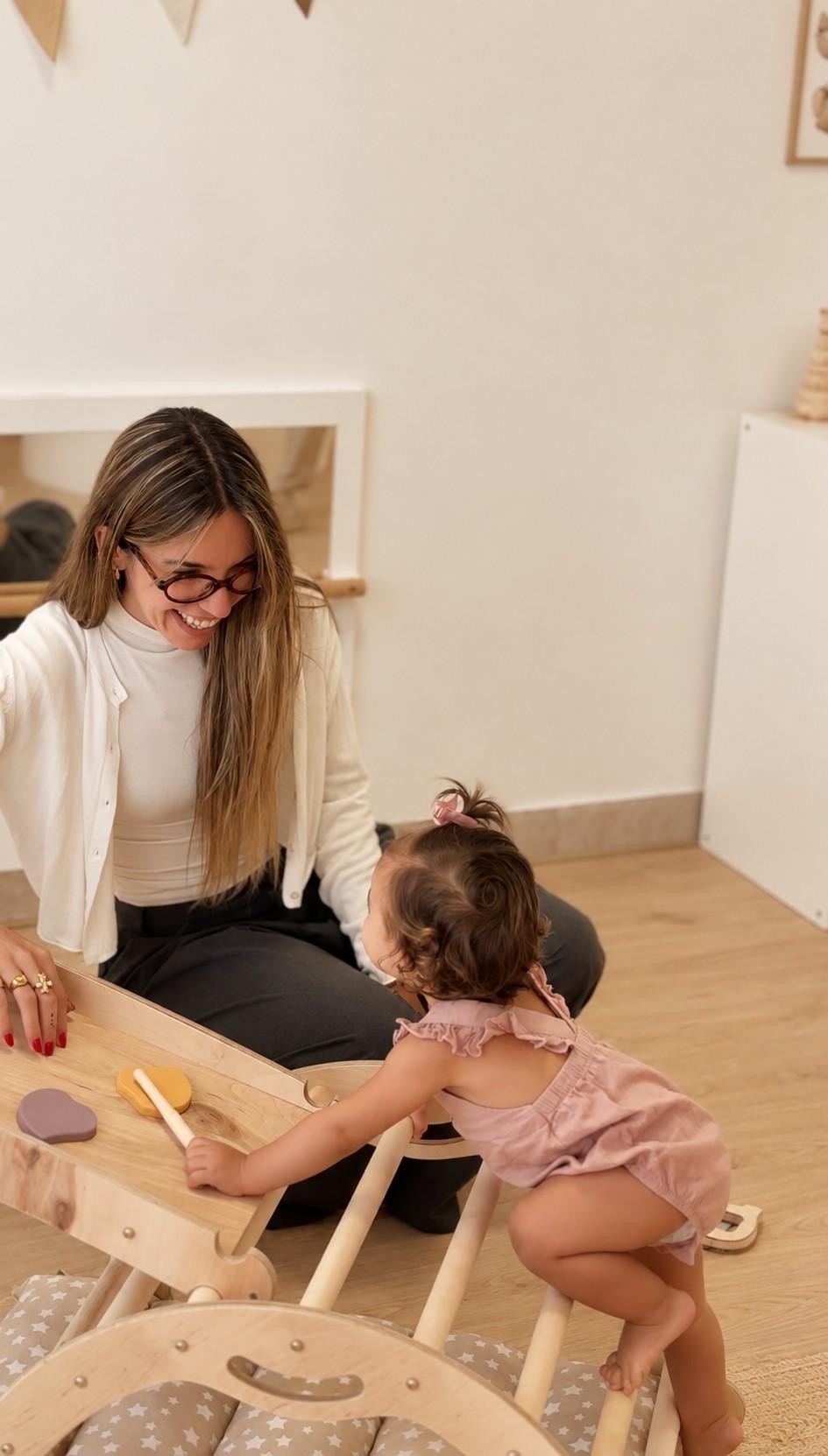 Una bebé trepa por un triángulo de madera acompañada por una educadora