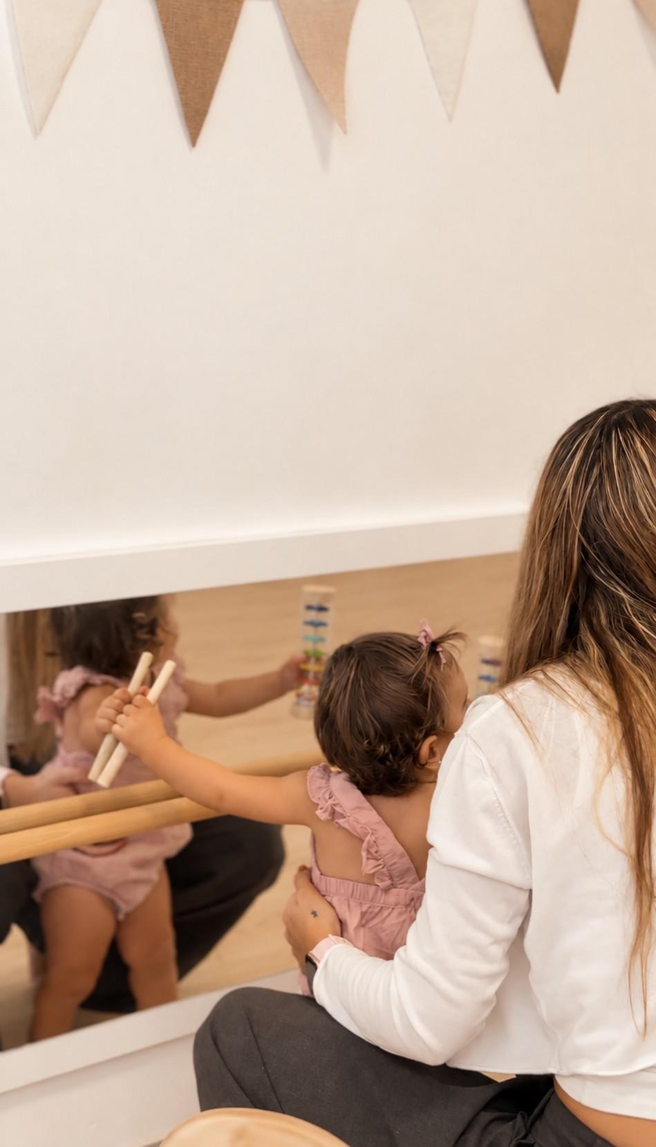 Una educadora juega con una bebé frente a un espejo