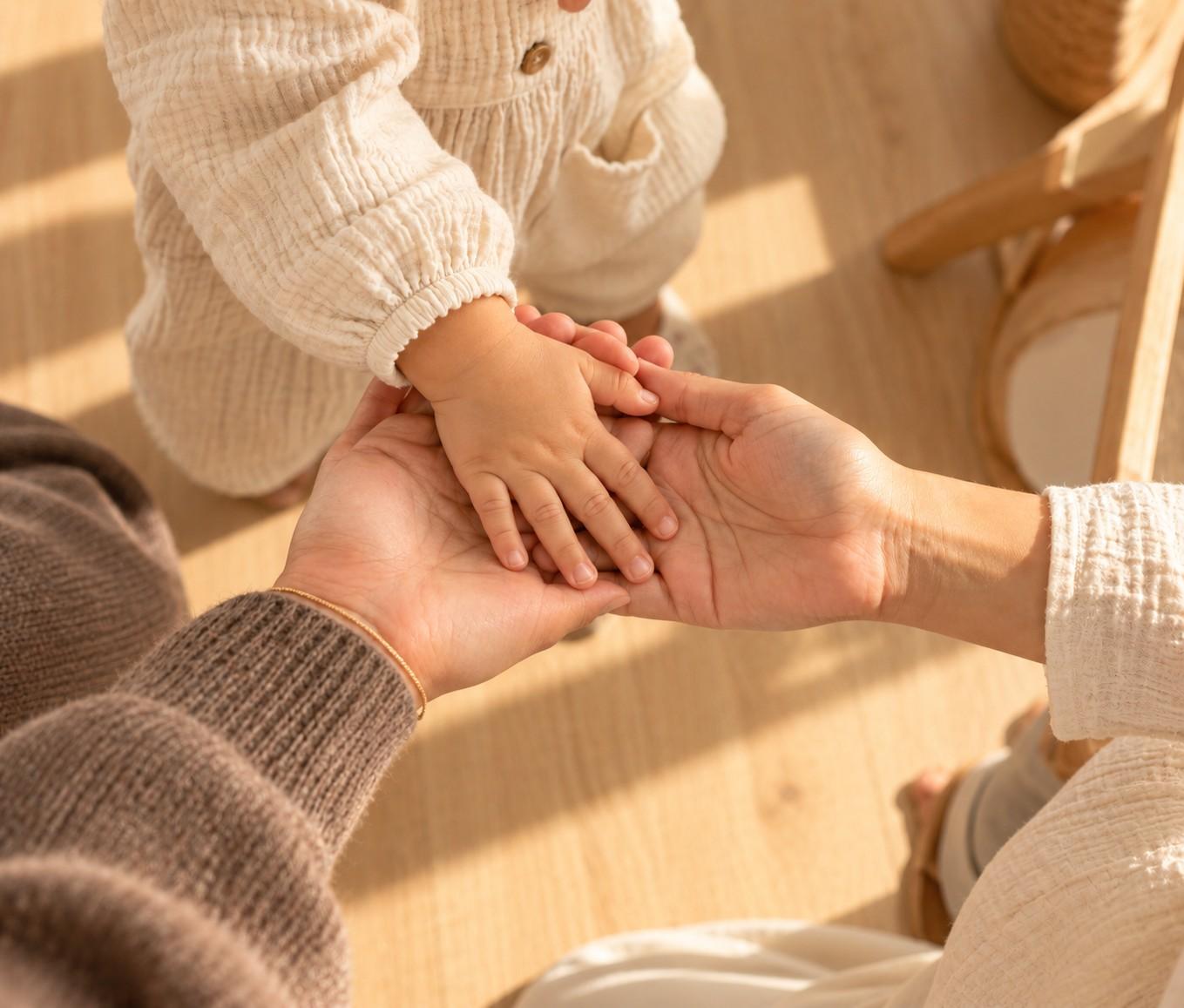 La mano de un bebé descansa sobre la mano de una educadora