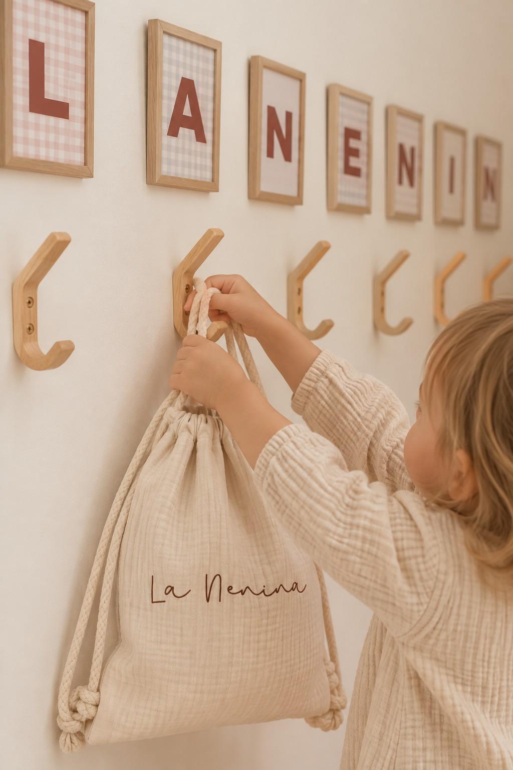 Una niña cuelga su mochila de La Nenina en las perchas de madera, bajo las letras del nombre